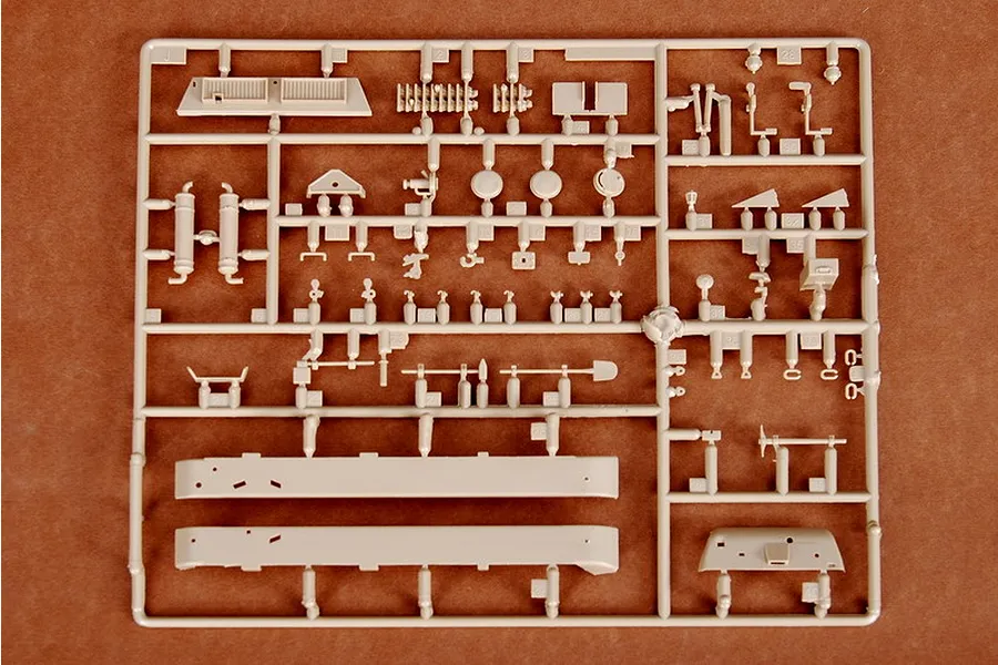 A plastic model kit sprue containing various small parts for a 1/35 scale German artillery vehicle, laid out on a brown surface.