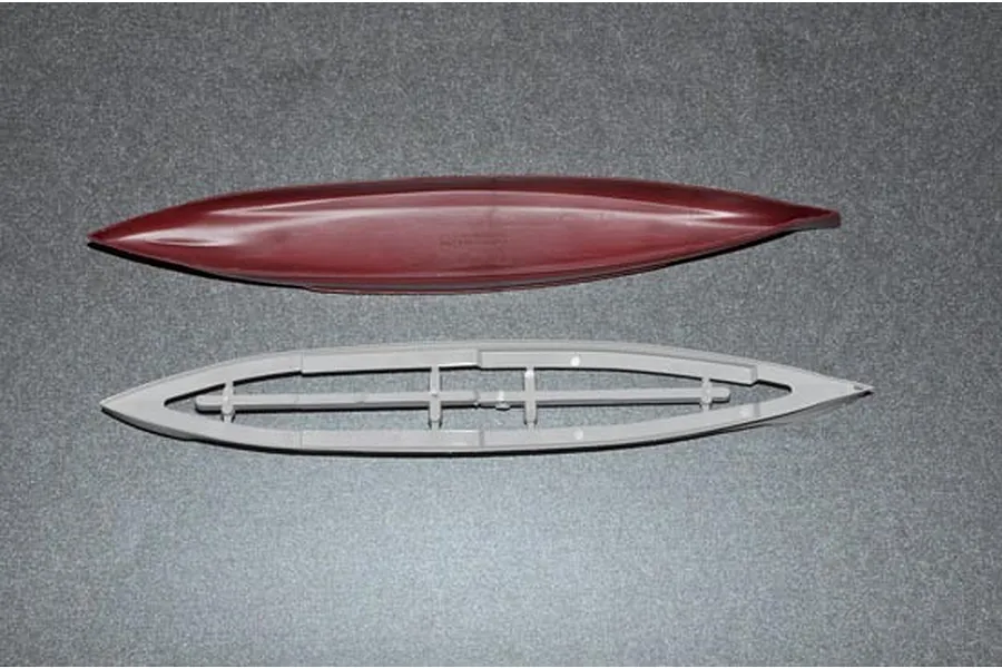 Top-down view of two plastic model ship hull components, one maroon and one grey, on a textured grey surface.