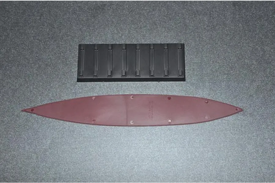 Top-down view of a plastic model ship hull piece and a black display stand on a grey surface.