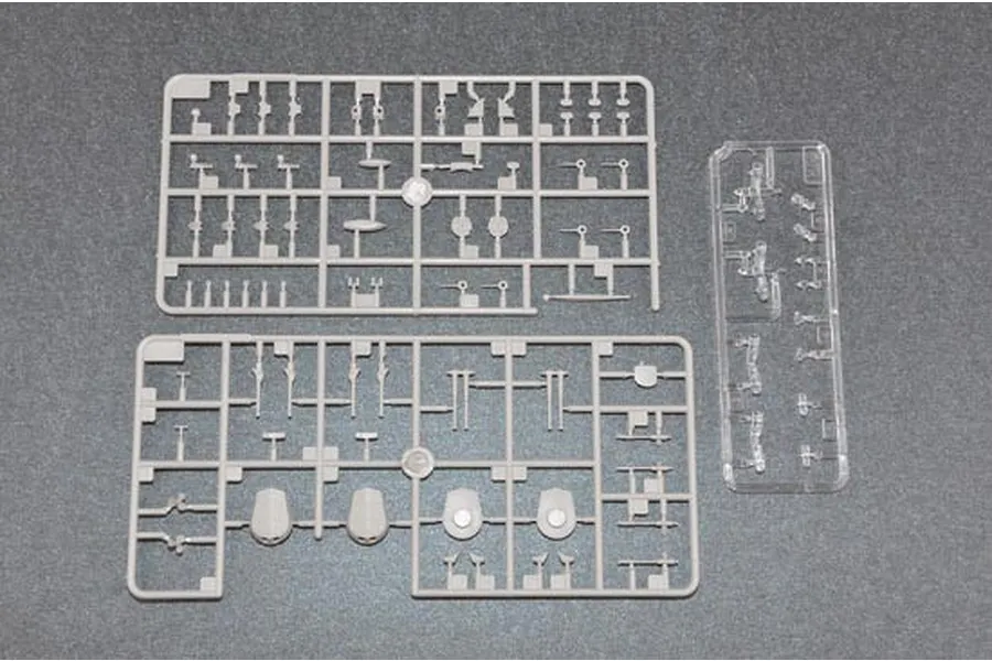 Two grey plastic model kit sprues and one clear plastic sprue containing small ship parts on a grey background.