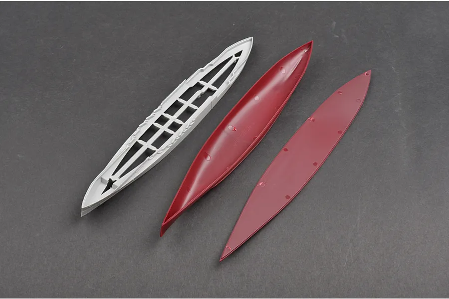 Three plastic model ship hull components laid out on a dark grey surface, including a grey deck piece and two red hull sections.