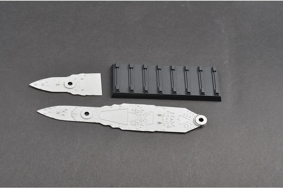 Unassembled plastic model ship deck pieces and a black display stand on a grey surface.
