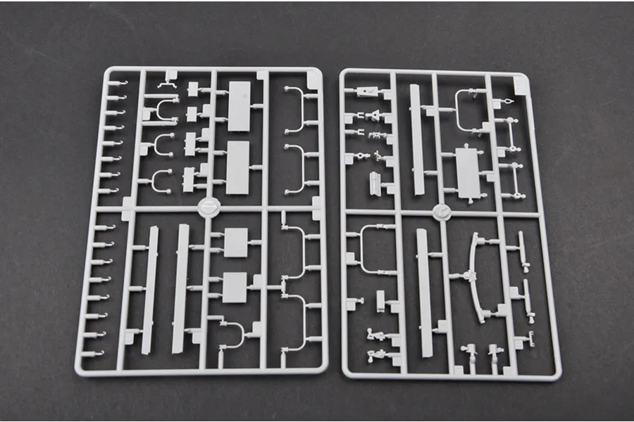 Two grey plastic model kit sprues containing various small vehicle parts laid out on a dark surface.