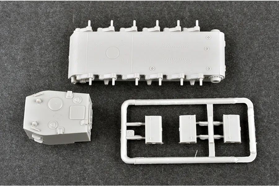 Unassembled grey plastic model kit parts for a tank, including the lower hull, turret, and a small sprue with three rectangular components.