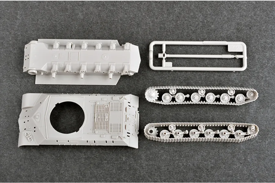 Top-down view of unpainted grey plastic model tank parts including the hull, turret base, and track assemblies on a dark grey background.