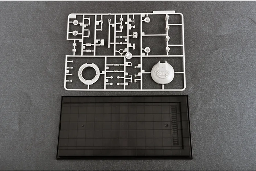 A plastic model kit sprue containing tank parts and a black display base on a grey background.