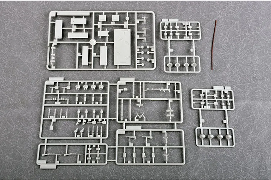 Four grey plastic model kit sprues and a thin brown wire on a grey textured surface.