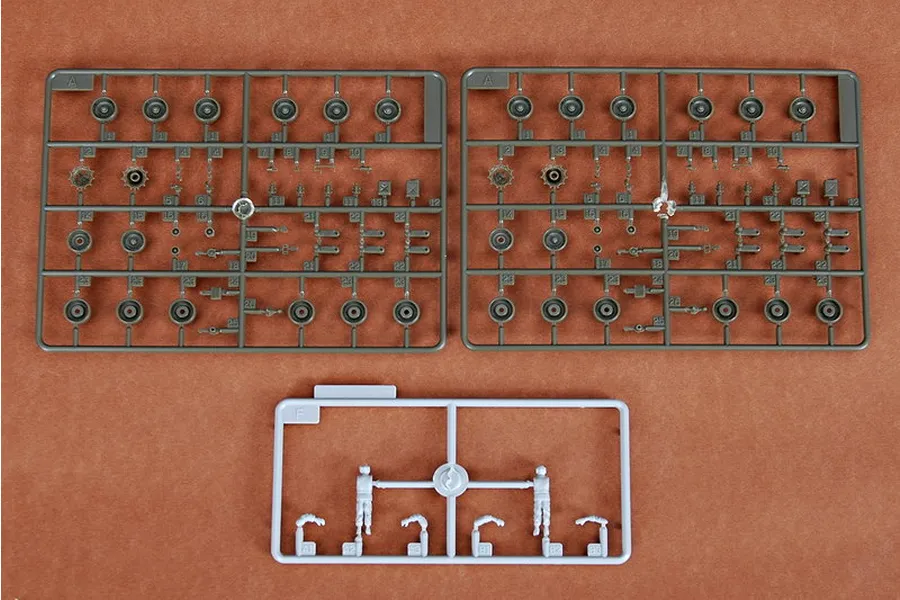 Plastic model kit sprues for a 1/72 scale tank, including two olive green sprues with wheels and a small light grey sprue with two tank crew figures.