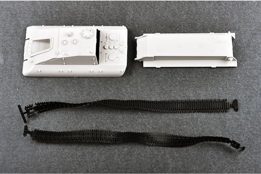 Unassembled plastic model kit parts for a Jagdpanzer E-100, including the upper hull, lower hull, and two flexible black tank tracks on a grey surface.