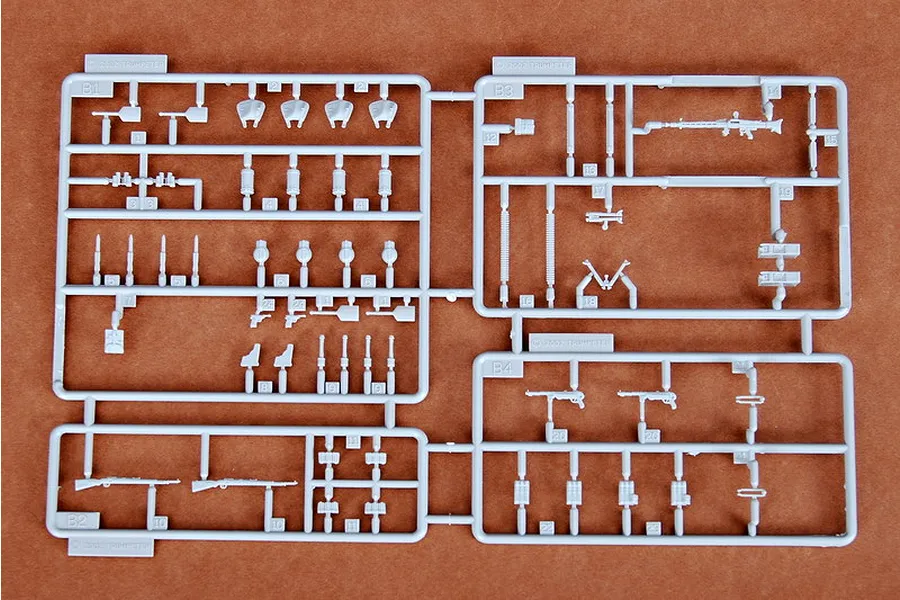 A grey plastic sprue containing various miniature military equipment parts for a 1/35 scale model kit, including rifles, machine guns, and tools.