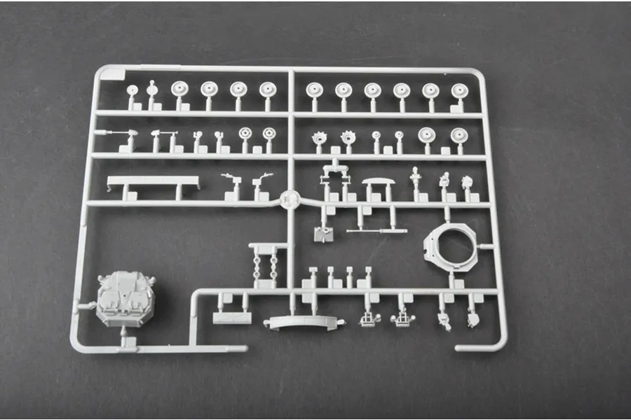 A grey plastic sprue containing various unpainted model tank parts, including wheels and turret components, against a dark grey background.