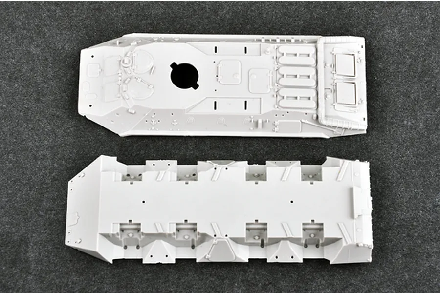 Top-down view of two unpainted grey plastic model kit parts for a BTR-70 APC, showing the upper hull and lower chassis on a dark textured surface.
