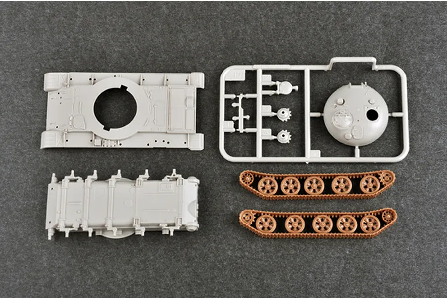 Plastic model tank parts including hull, turret on sprue, and two track assemblies on a grey background.