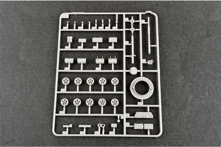 A grey plastic model kit sprue containing various tank parts including road wheels, fuel drums, and structural components on a dark grey background.