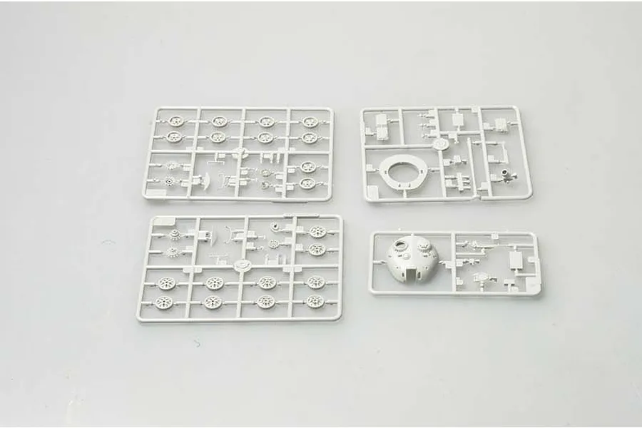 Four grey plastic model kit sprues containing tank parts, including road wheels and a turret, laid out on a plain light grey background.