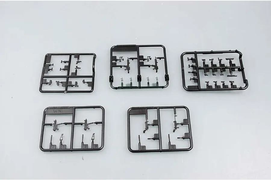 Five black plastic model kit sprues containing miniature firearm parts on a light grey background.