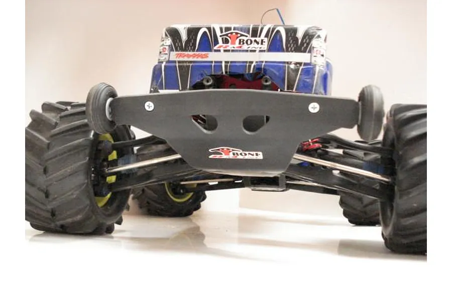 A close-up, low-angle view of a T-Bone Racing black rear bumper installed on a Traxxas E-Maxx RC monster truck, featuring integrated wheelie wheels.
