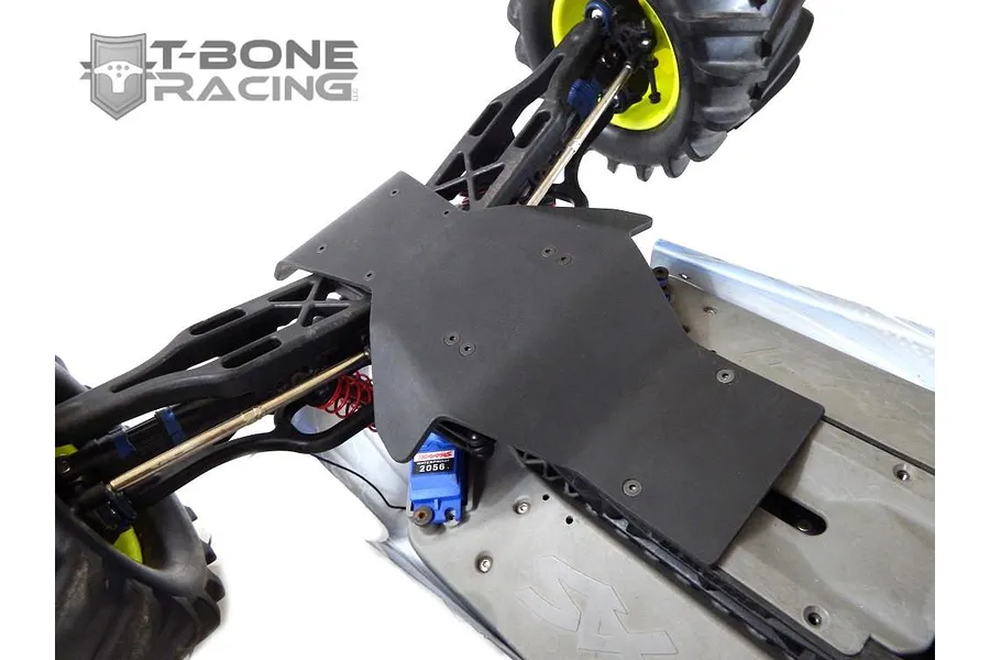 A black T-Bone Racing skid plate installed on the chassis of a Traxxas E-Maxx RC truck, showing the front suspension and steering servo.