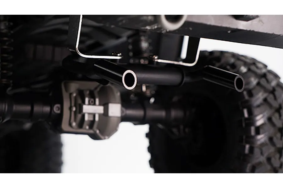 A close-up view of a black metal dual exhaust pipe accessory installed on the underside of an RC crawler chassis.