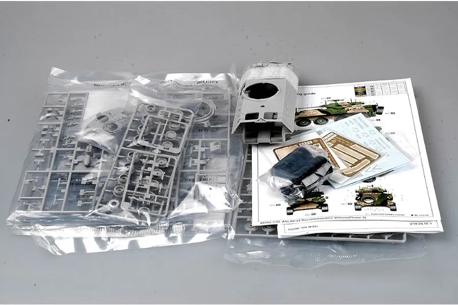 Contents of a Trumpeter 1/35 ASLAV-25 model kit, including grey plastic sprues in bags, a hull piece, decal sheet, and instruction manual.