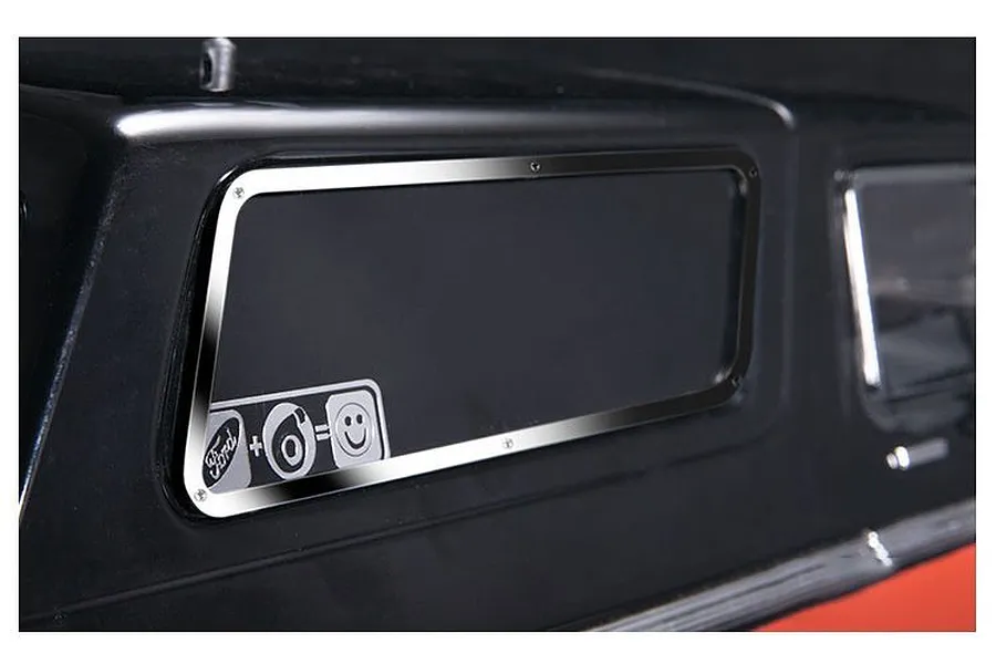 Close-up of a shiny stainless steel window trim installed on a black RC car body, featuring a small Ford logo and smiley face graphic on the window.
