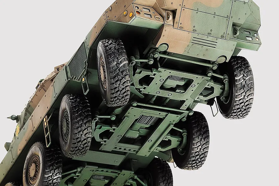 Low angle view of the underside of a Tamiya 1/35 JGSDF Type 16 Combat Vehicle model kit, showing the suspension, wheels, and chassis detail.