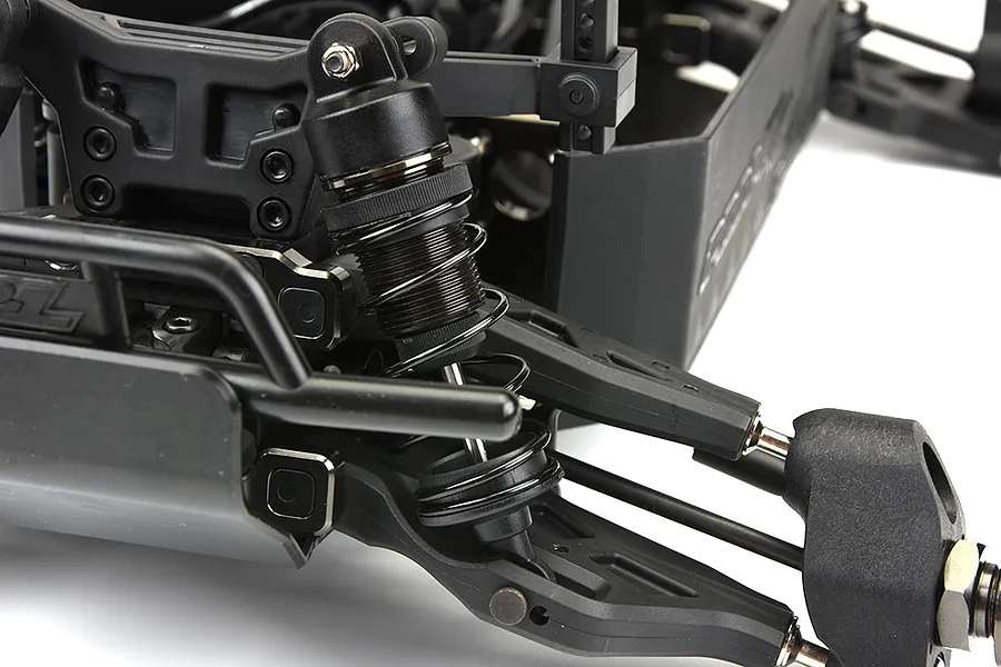 Close-up of the front suspension assembly on a Pro-Line PRO-MT RC monster truck roller, showing the shock absorber, control arm, and chassis components.