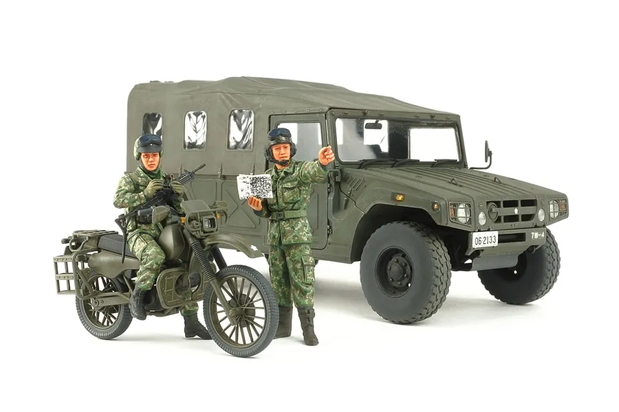 A 1/35 scale Tamiya model kit featuring a JGSDF High Mobility Vehicle, a reconnaissance motorcycle, and two soldier figures in camouflage uniforms.