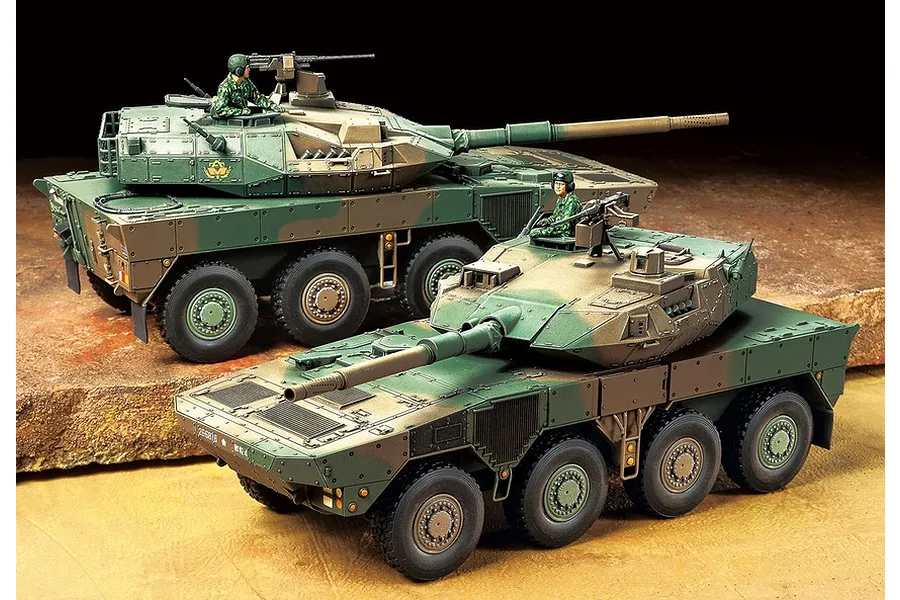 Two assembled and painted 1/48 scale JGSDF Type 16 combat vehicle models displayed on a textured ground surface.