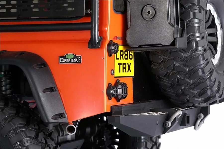Close-up of the rear corner of an orange RC Land Rover Defender showing black GPM tail light guards installed over the lights.