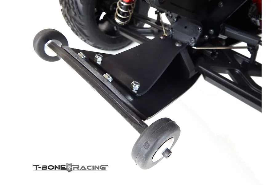 A T-Bone Racing wheelie bar installed on the rear of an ARRMA Kraton RC truck, featuring a black plastic skid plate and two small rubber wheels.