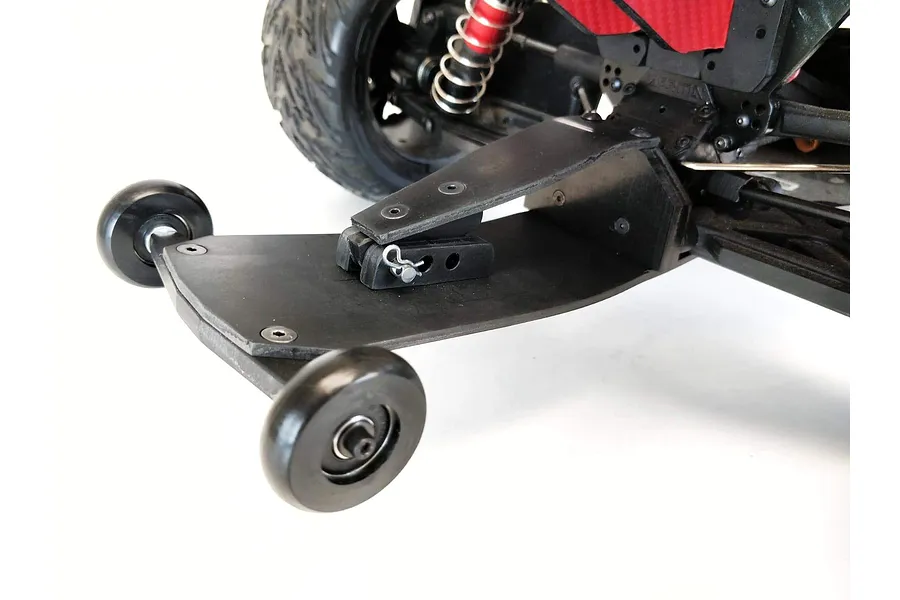 A black T-Bone Racing wheelie bar installed on the rear of an ARRMA Typhon RC buggy, featuring two small black wheels and a flat mounting plate.