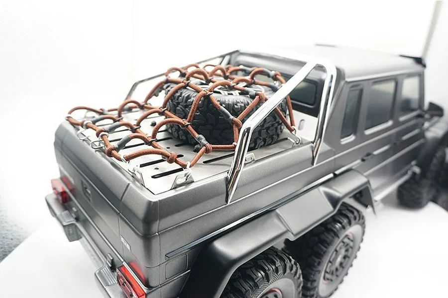 A stainless steel tray cover and brown cargo net installed on the rear bed of a grey Traxxas TRX-6 Mercedes-Benz G 63 AMG 6x6 RC crawler.