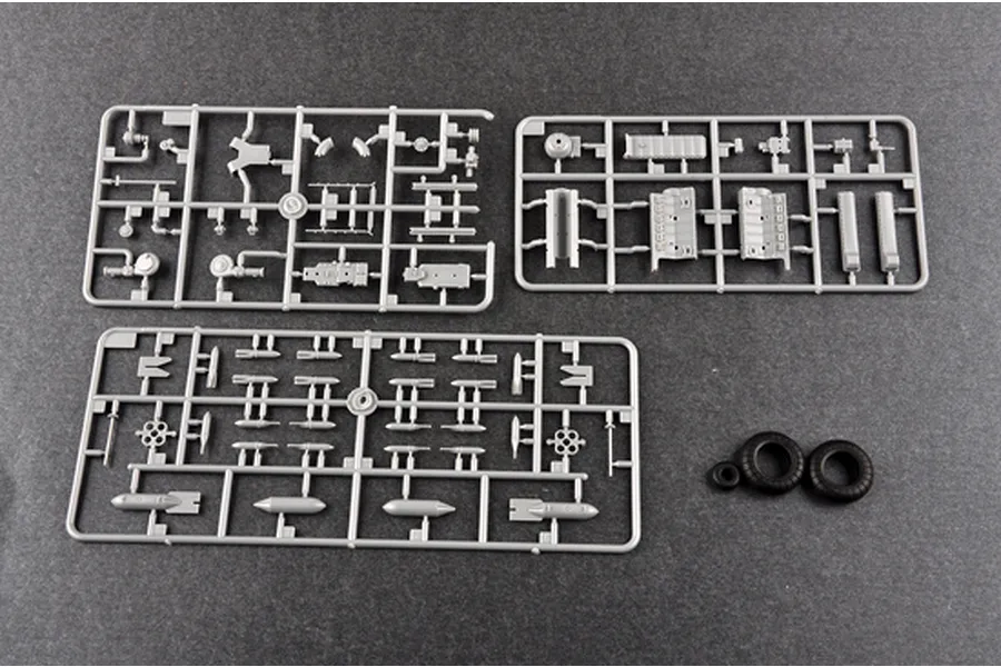 Three grey plastic model kit sprues and three black rubber tires laid out on a dark grey surface.