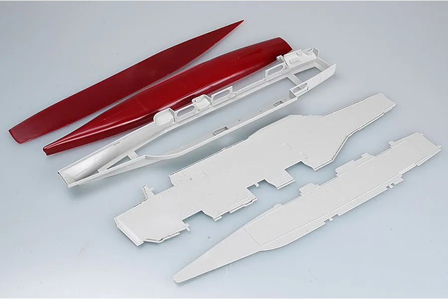 Unassembled plastic model kit parts for an aircraft carrier, including a red hull and grey deck sections on a white background.