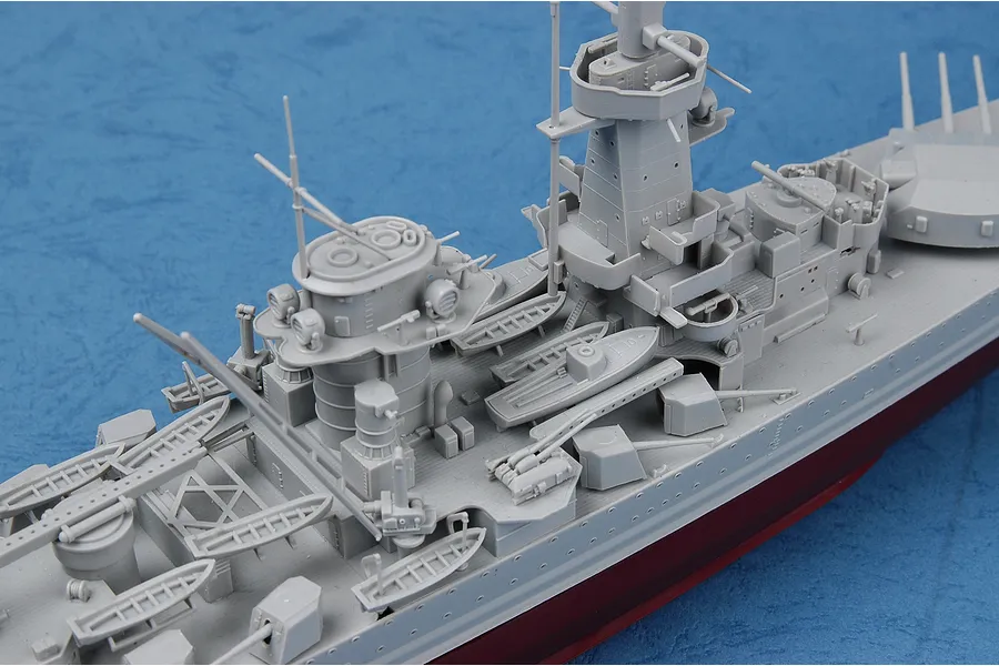 A high-angle close-up of an unpainted grey plastic model battleship deck showing detailed superstructure, masts, and small lifeboats.