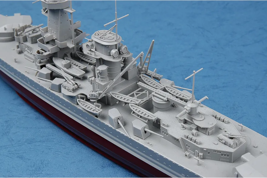 A high-angle close-up of a partially assembled grey plastic model battleship on a blue textured background.