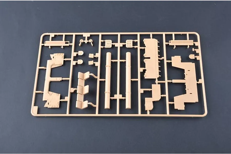 A tan plastic sprue containing various model tank parts, including two long cylindrical pieces, against a dark grey background.