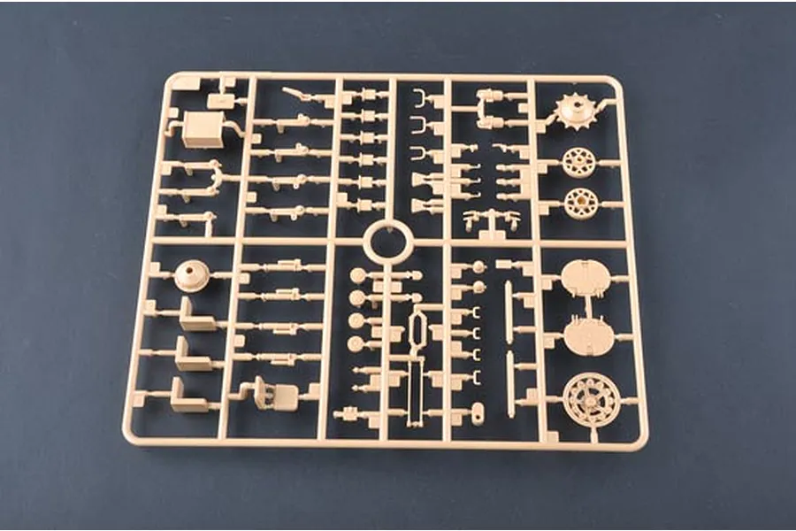 A beige plastic model kit sprue containing various tank parts, including wheels and suspension components, against a dark grey background.