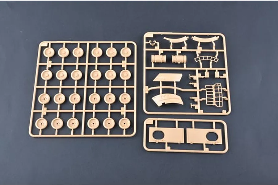 Three plastic model kit sprues containing tank wheels and various structural parts on a dark grey background.