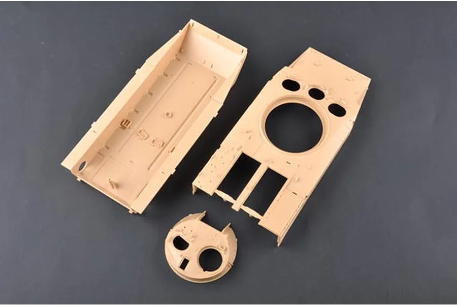 Unassembled plastic model tank hull and turret parts in tan plastic on a dark grey background.