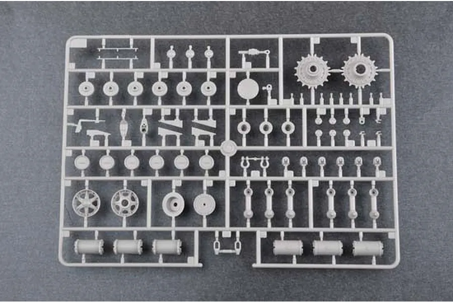 A grey plastic sprue containing various model tank parts, including road wheels, sprockets, and suspension components, viewed from above.