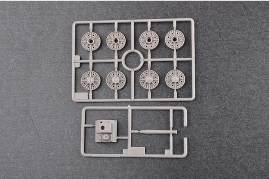 Two grey plastic model kit sprues containing tank road wheels and a small turret component on a dark grey background.