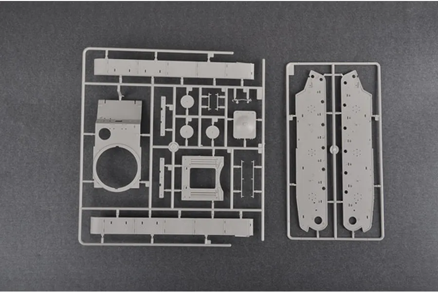Two grey plastic model kit sprues containing tank parts, including hull sides and turret components, laid out on a dark grey background.