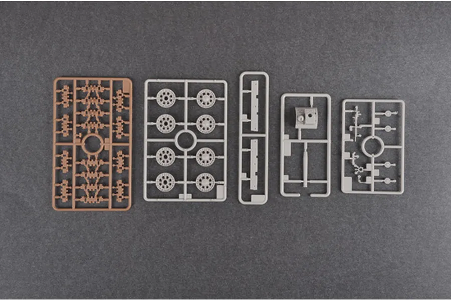 Five plastic model kit sprues for a 1/35 scale tank, including wheels, turret parts, and suspension components, laid out on a dark grey surface.