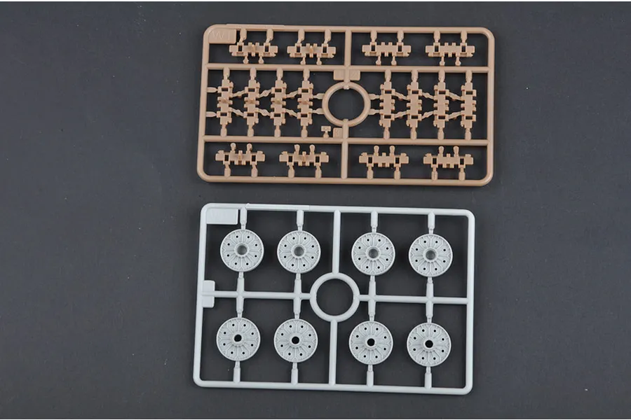 Two plastic model kit sprues on a dark background, one tan with small track links and one grey with eight circular road wheels.