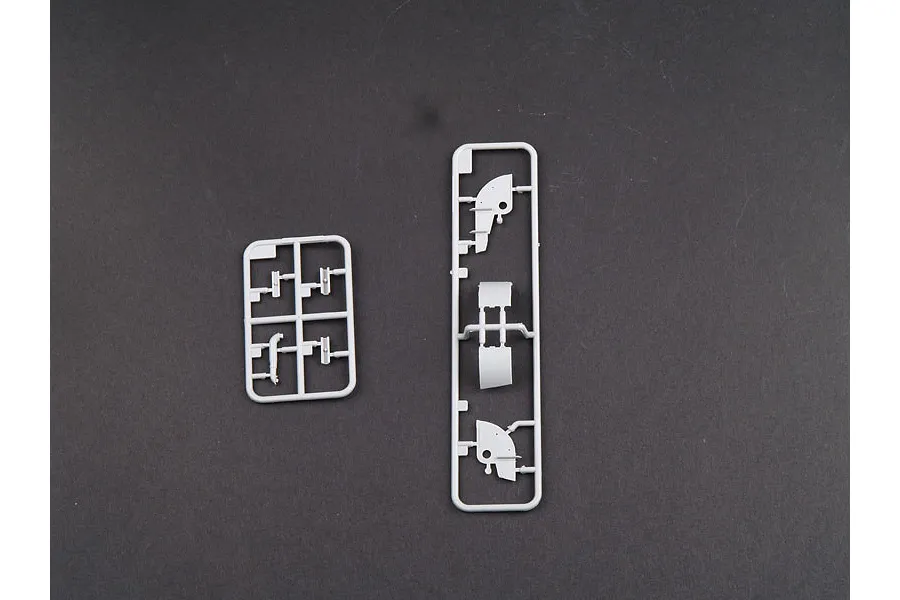 Two grey plastic model kit sprues containing small tank parts against a dark grey background.