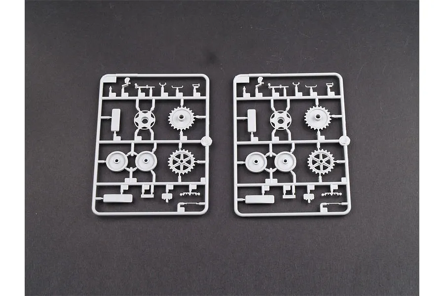 Two identical grey plastic model kit sprues featuring tank wheels and small mechanical parts on a dark grey background.