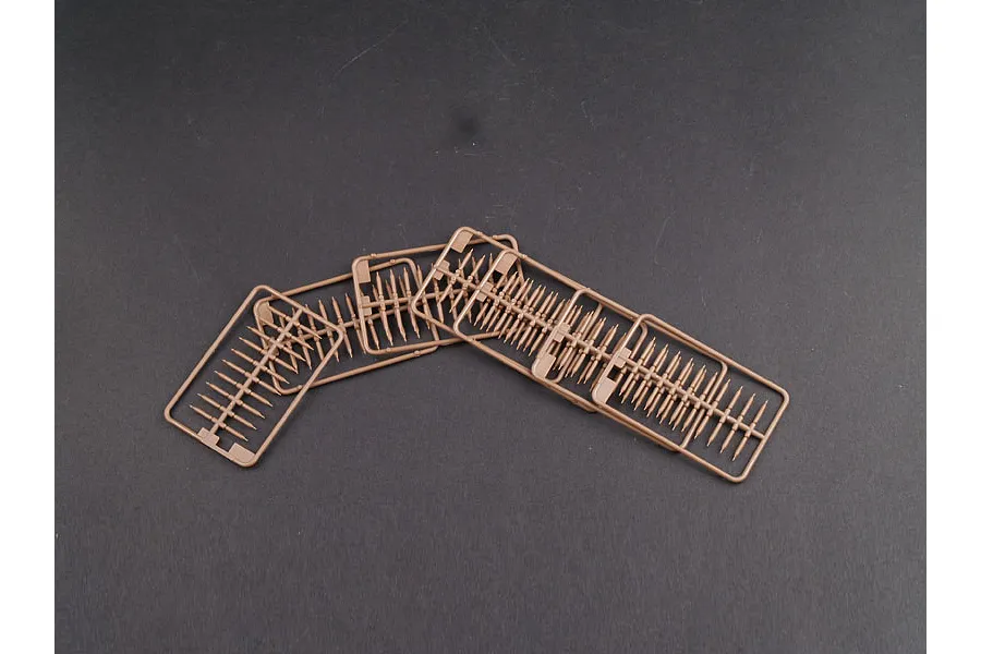 Three tan plastic model kit sprues containing numerous small, identical rod-like parts on a dark grey background.