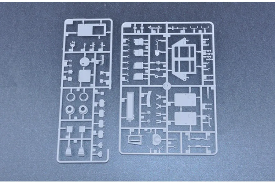 Two grey plastic model kit sprues containing various vehicle parts laid out on a dark surface.